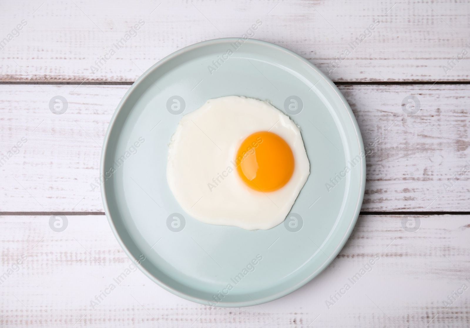 Photo of Tasty fried egg in plate on white wooden table, top view