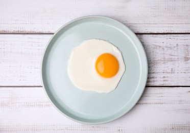 Tasty fried egg in plate on white wooden table, top view