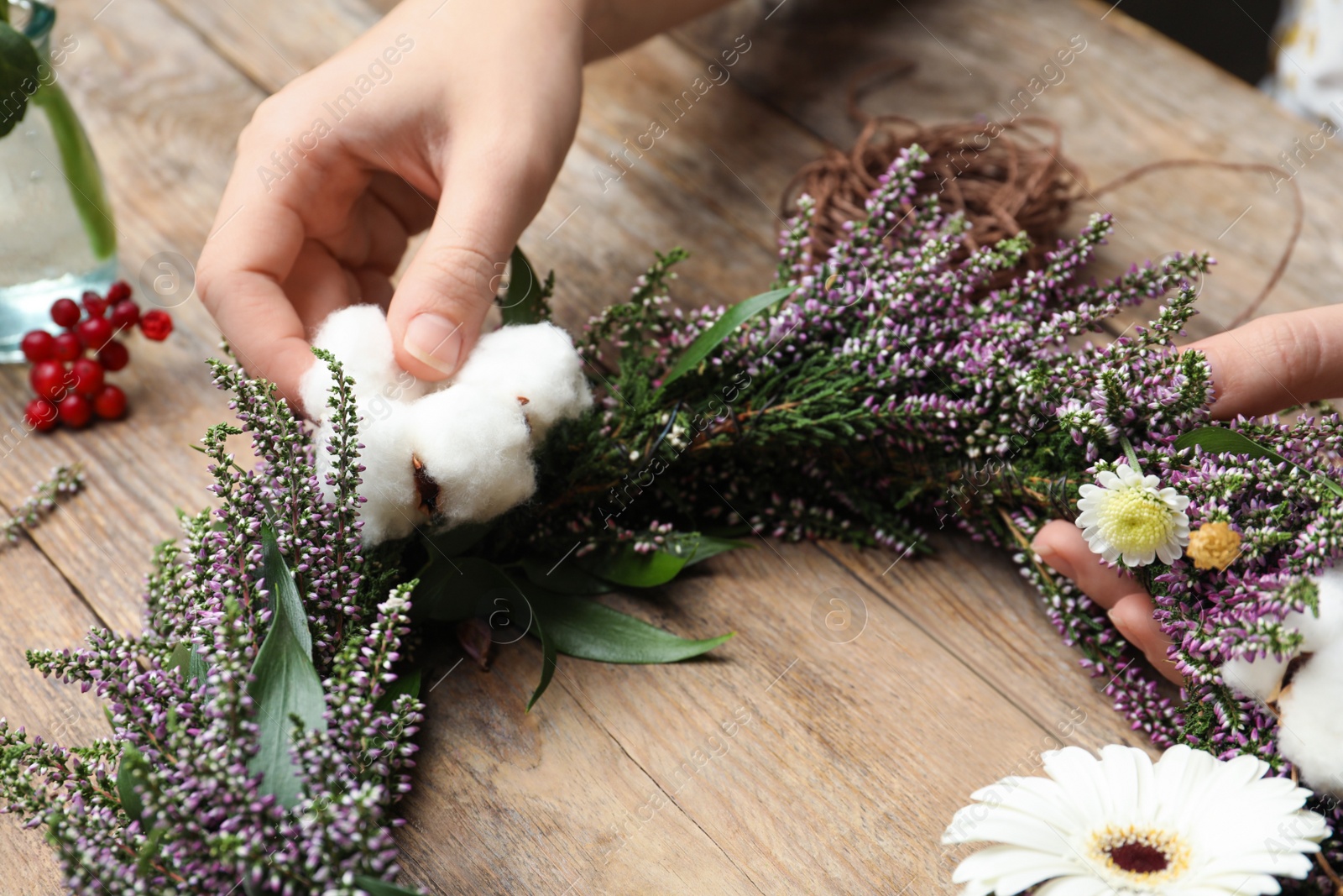 Photo of Florist making beautiful autumnal wreath with heather flowers at wooden table, closeup