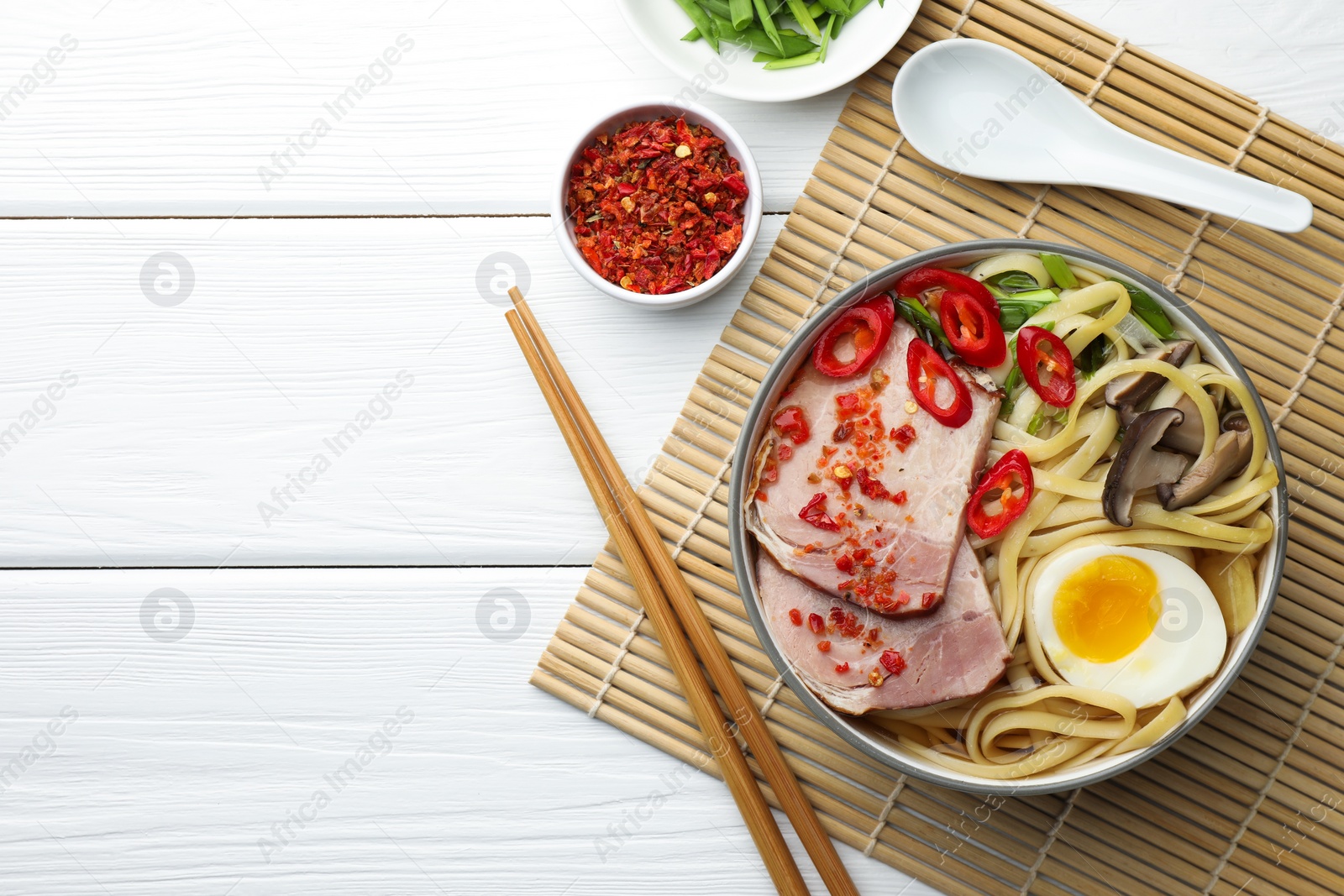 Photo of Delicious ramen in bowl served on white wooden table, flat lay and space for text. Noodle soup