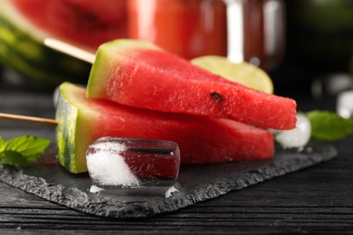 Photo of Slate board with juicy watermelon, ice and lime on black wooden table, closeup