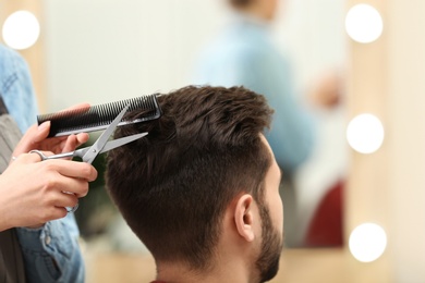 Photo of Barber making stylish haircut with professional scissors in beauty salon, closeup