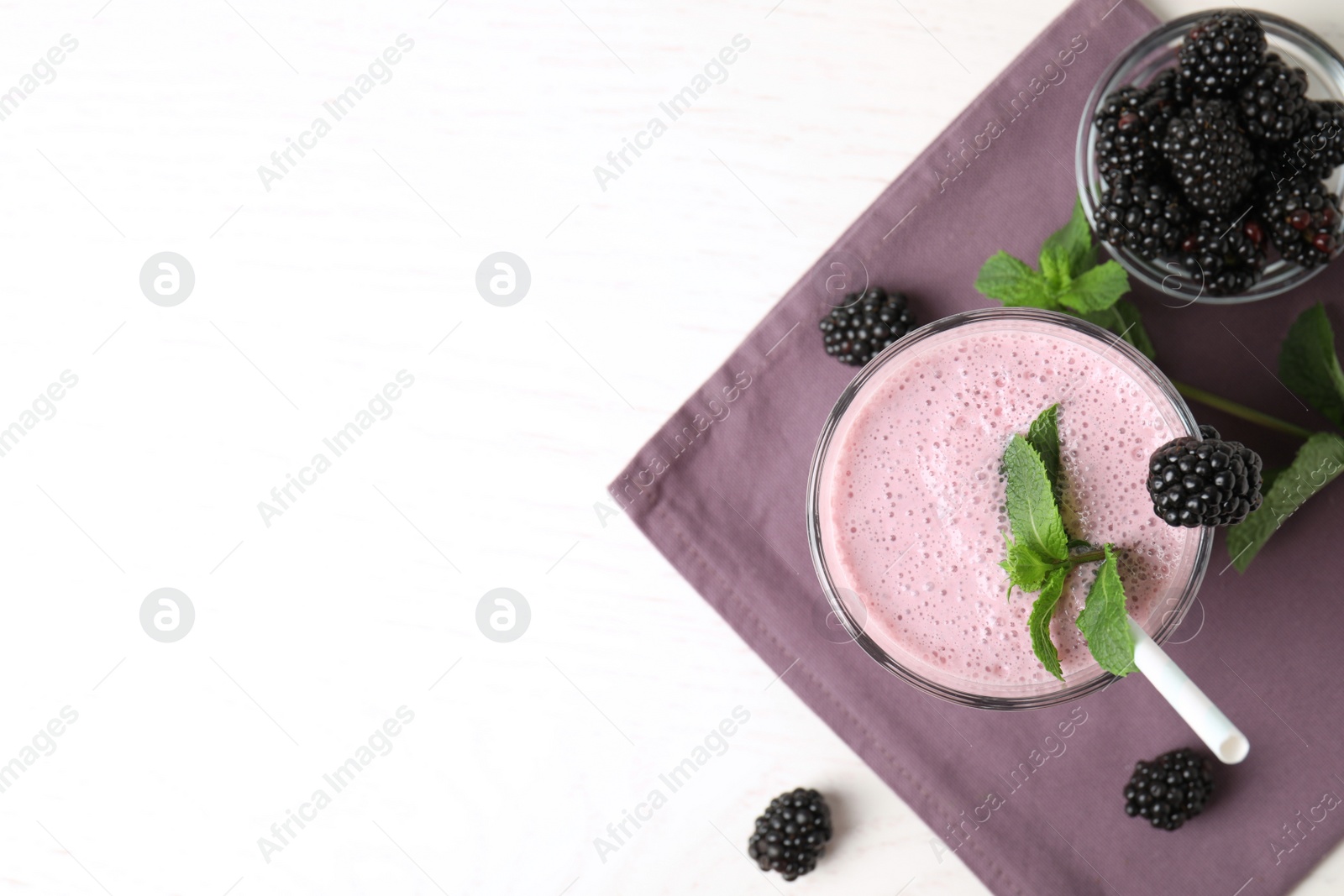 Photo of Tasty milk shake with blackberries on white table, flat lay. Space for text