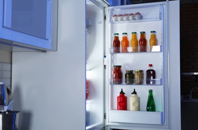 Photo of Open refrigerator full of products in stylish kitchen interior at night