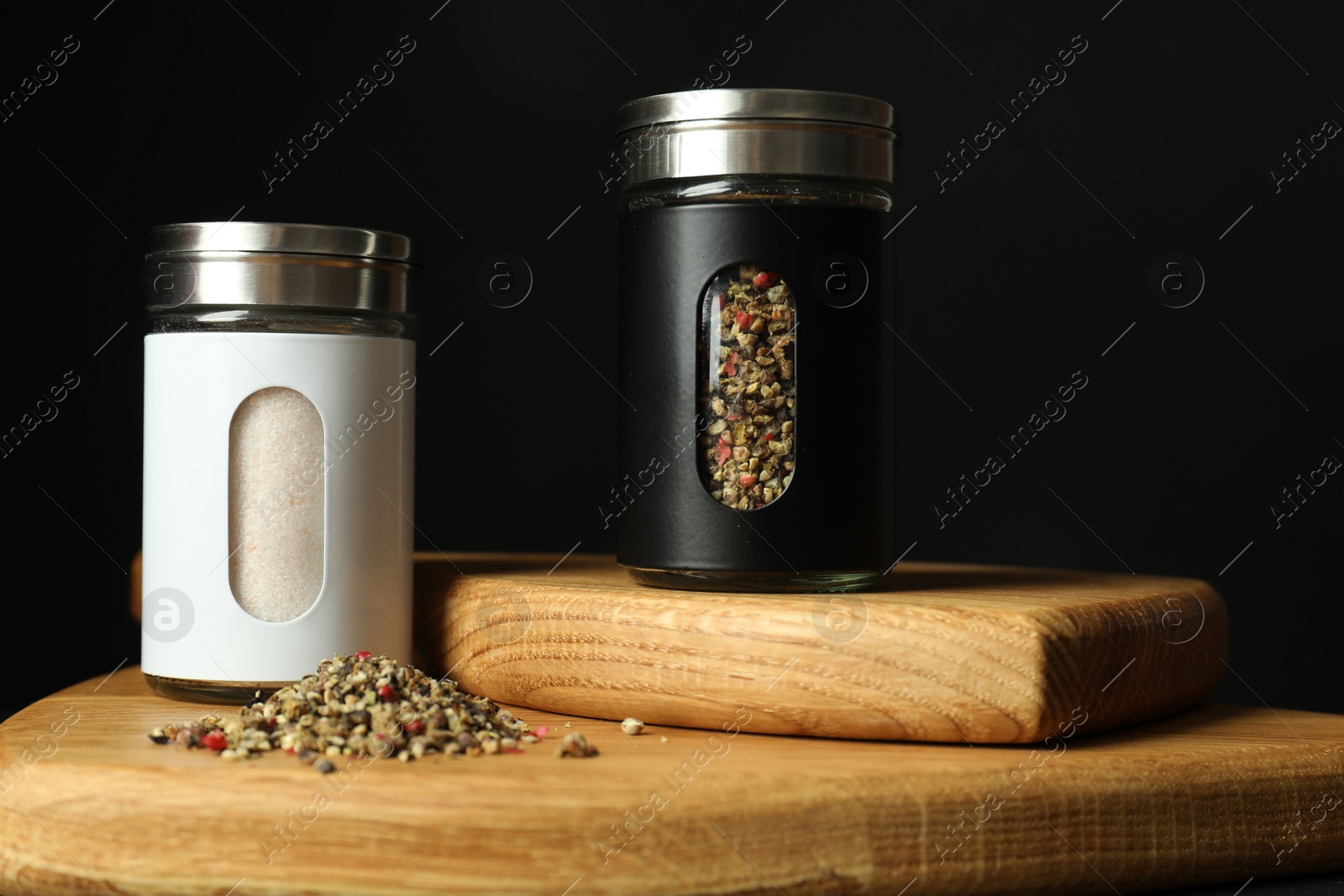 Photo of Salt and pepper shakers on wooden board against black background