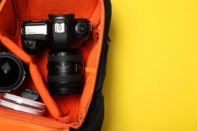 Photo of Camera in photographer's backpack on yellow background, top view. Space for text