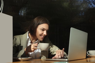 Special Promotion. Happy young woman with cup of drink using laptop at table in cafe