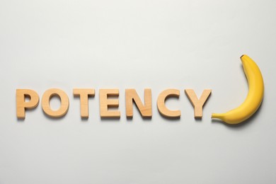 Photo of Word Potency made of wooden letters and banana on light grey background, flat lay