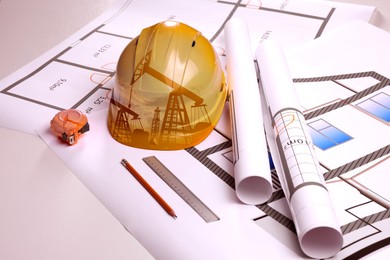 Image of Double exposure of crude oil pumps and hard hat on table with construction drawings