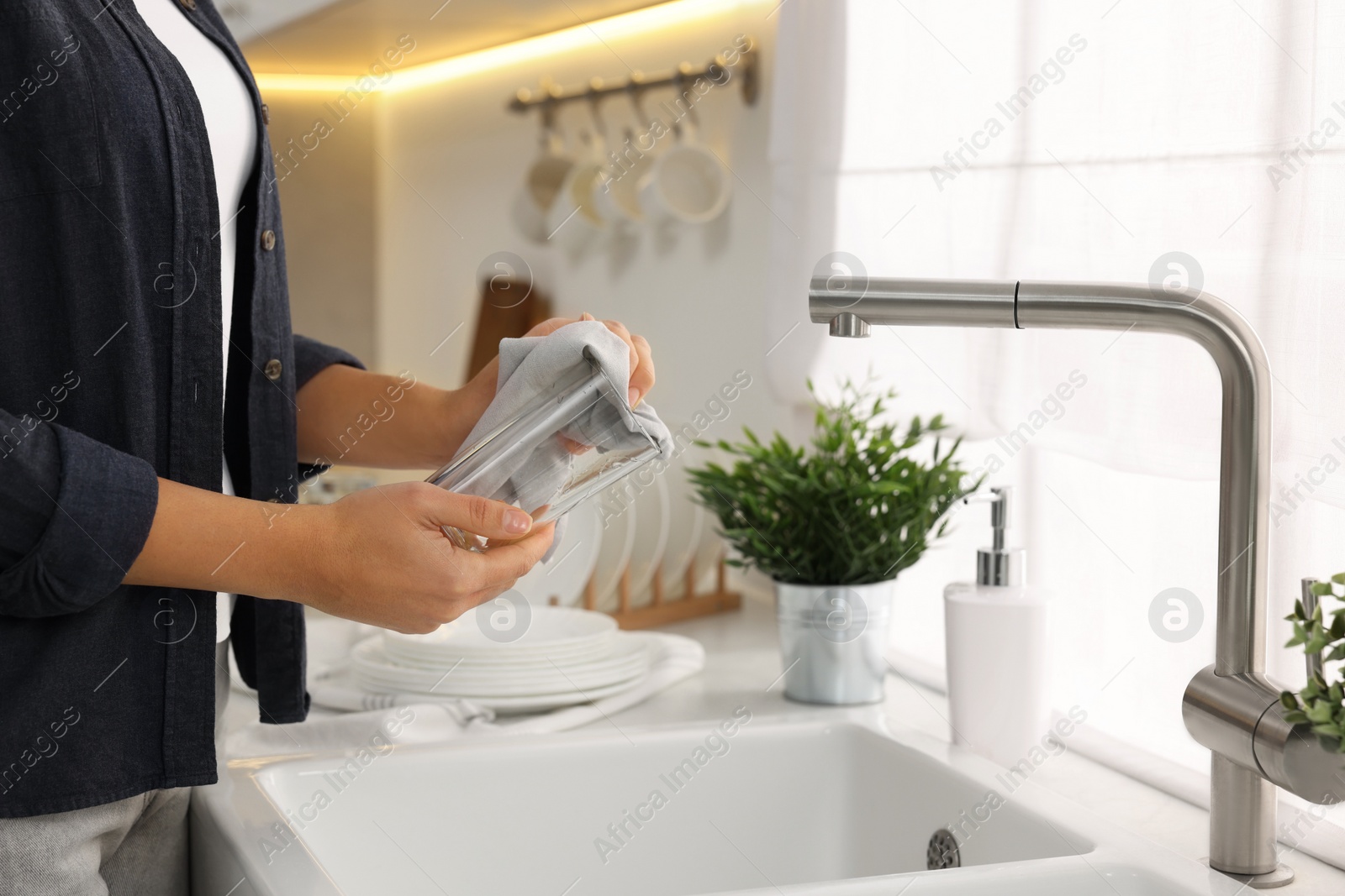 Photo of Woman wiping glass with towel in kitchen, closeup