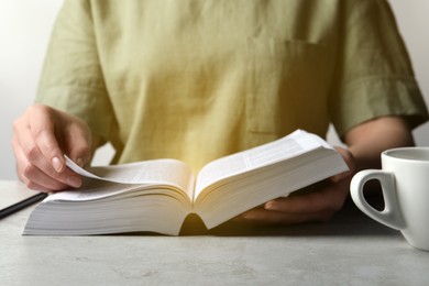 Photo of Woman reading holy Bible at grey textured table, closeup
