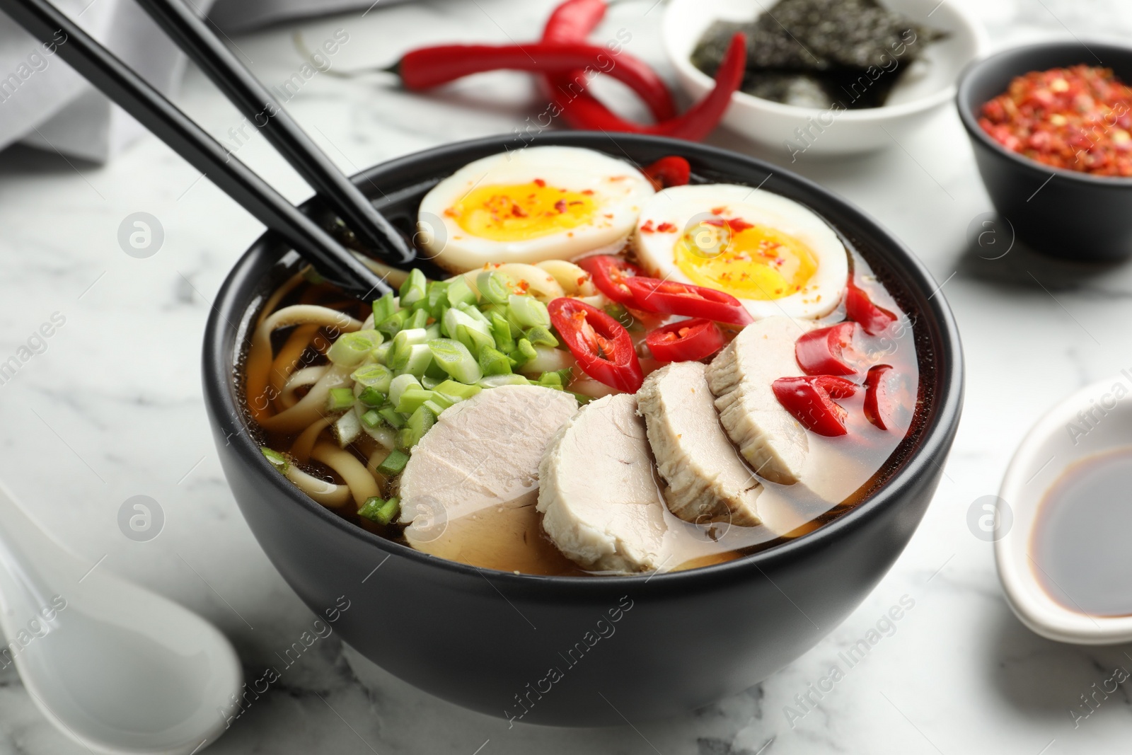 Photo of Delicious ramen in bowl on white marble table, closeup. Noodle soup