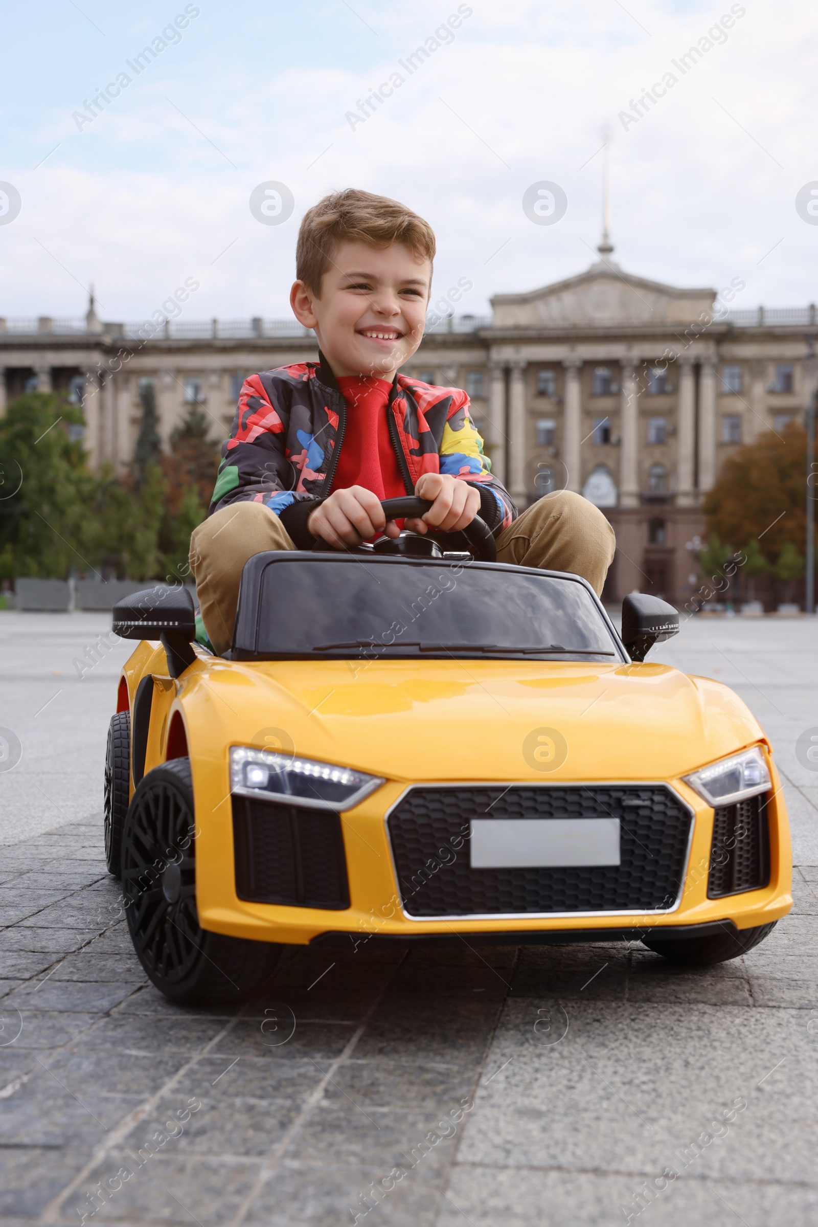 Photo of Cute little boy driving children's car on city street