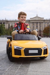 Cute little boy driving children's car on city street