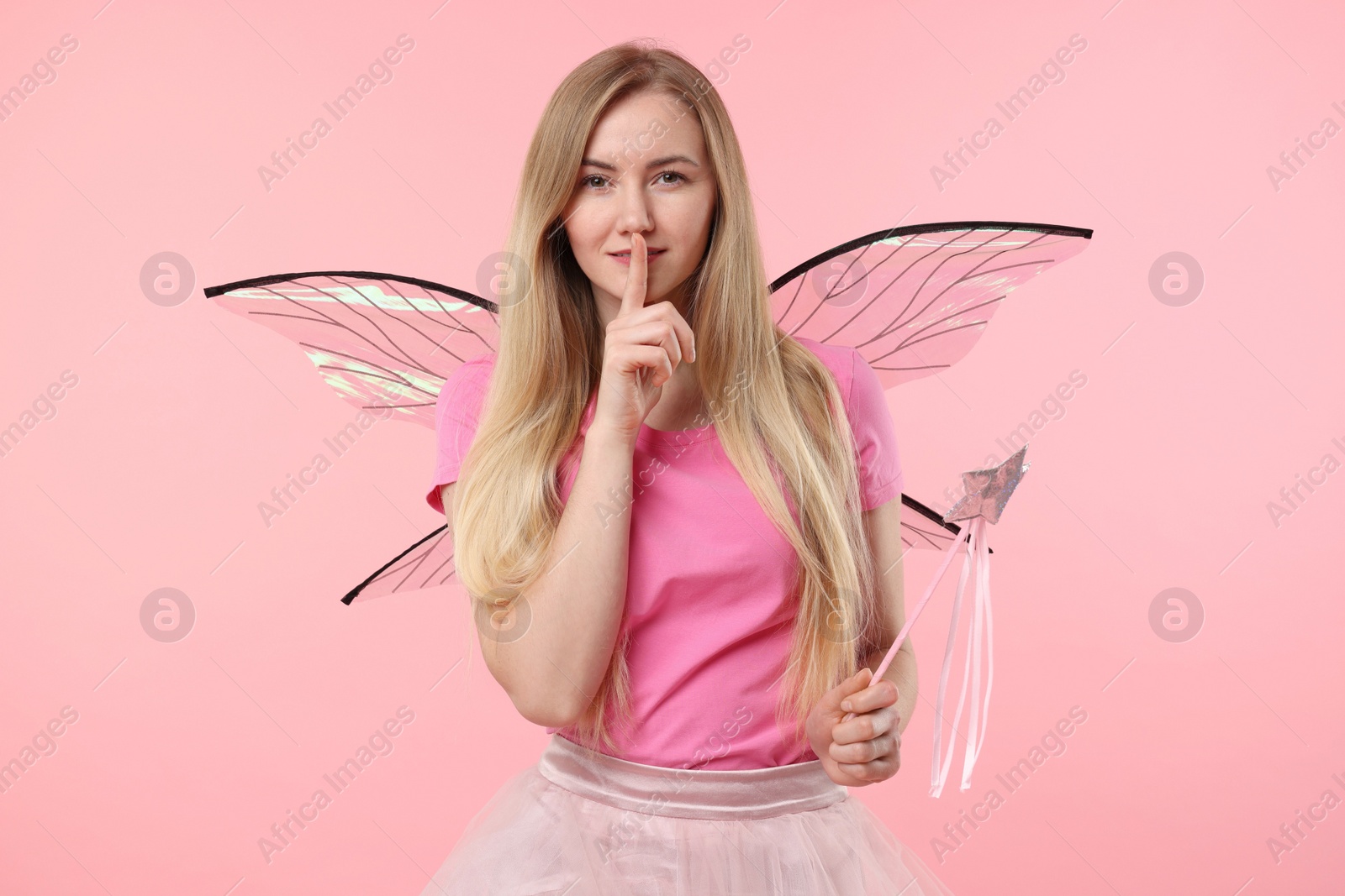 Photo of Beautiful girl in fairy costume with wings and magic wand on pink background