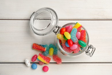 Photo of Jar with different delicious candies on white wooden table, flat lay