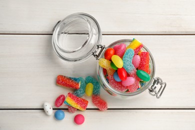 Jar with different delicious candies on white wooden table, flat lay