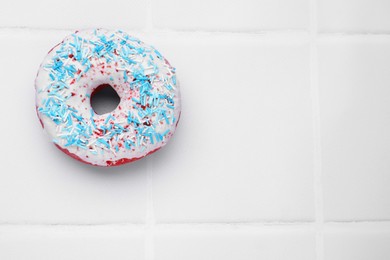 Photo of Glazed donut decorated with sprinkles on white tiled table, top view. Space for text. Tasty confectionery