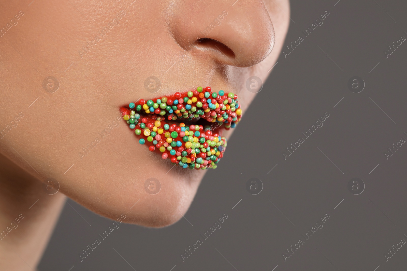 Photo of Young woman with beautiful lips covered confectionery sprinkles on gray background, closeup