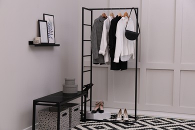 Photo of Rack with stylish women's clothes and bench in dressing room