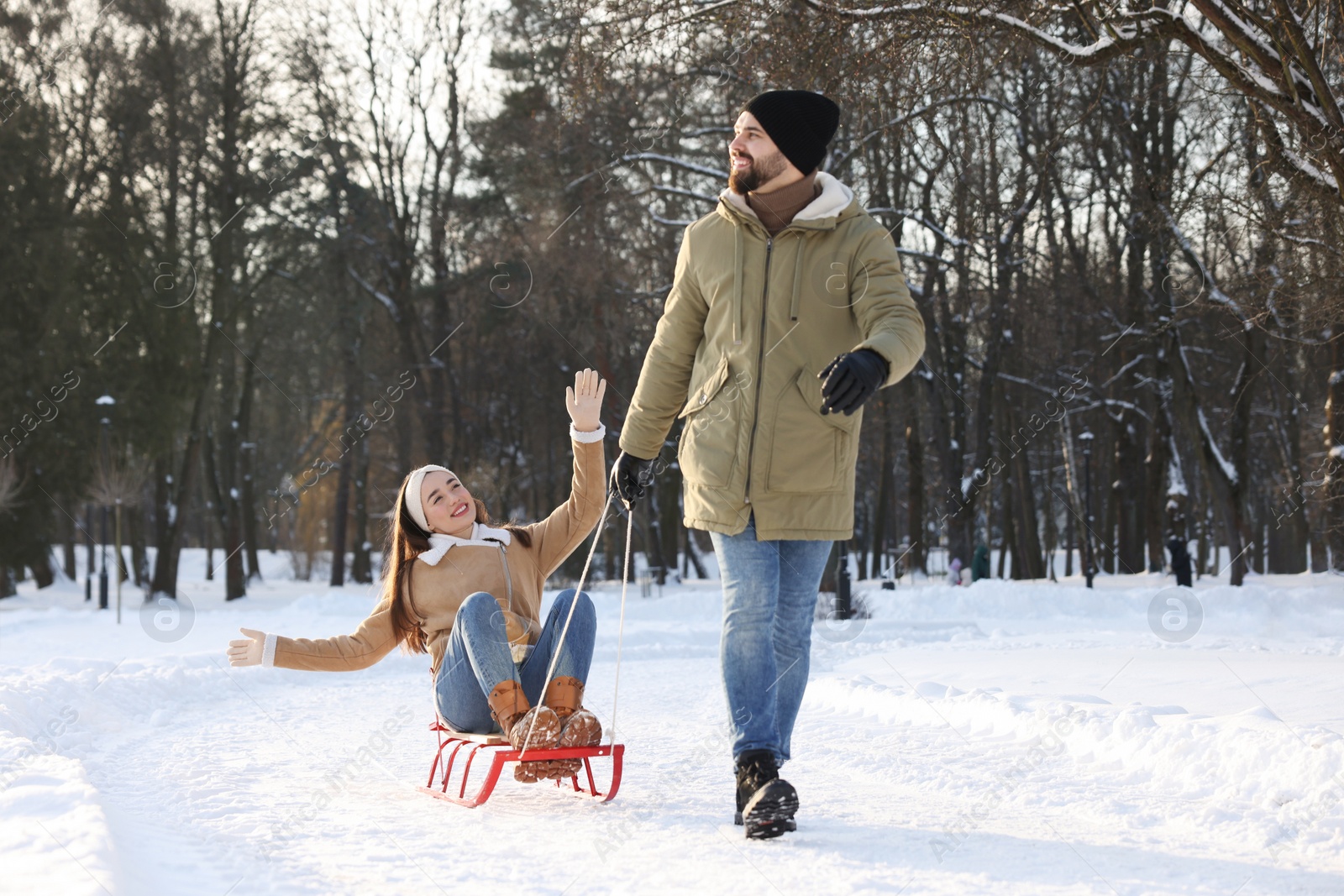 Photo of Happy young man pulling his girlfriend in sleigh outdoors on winter day