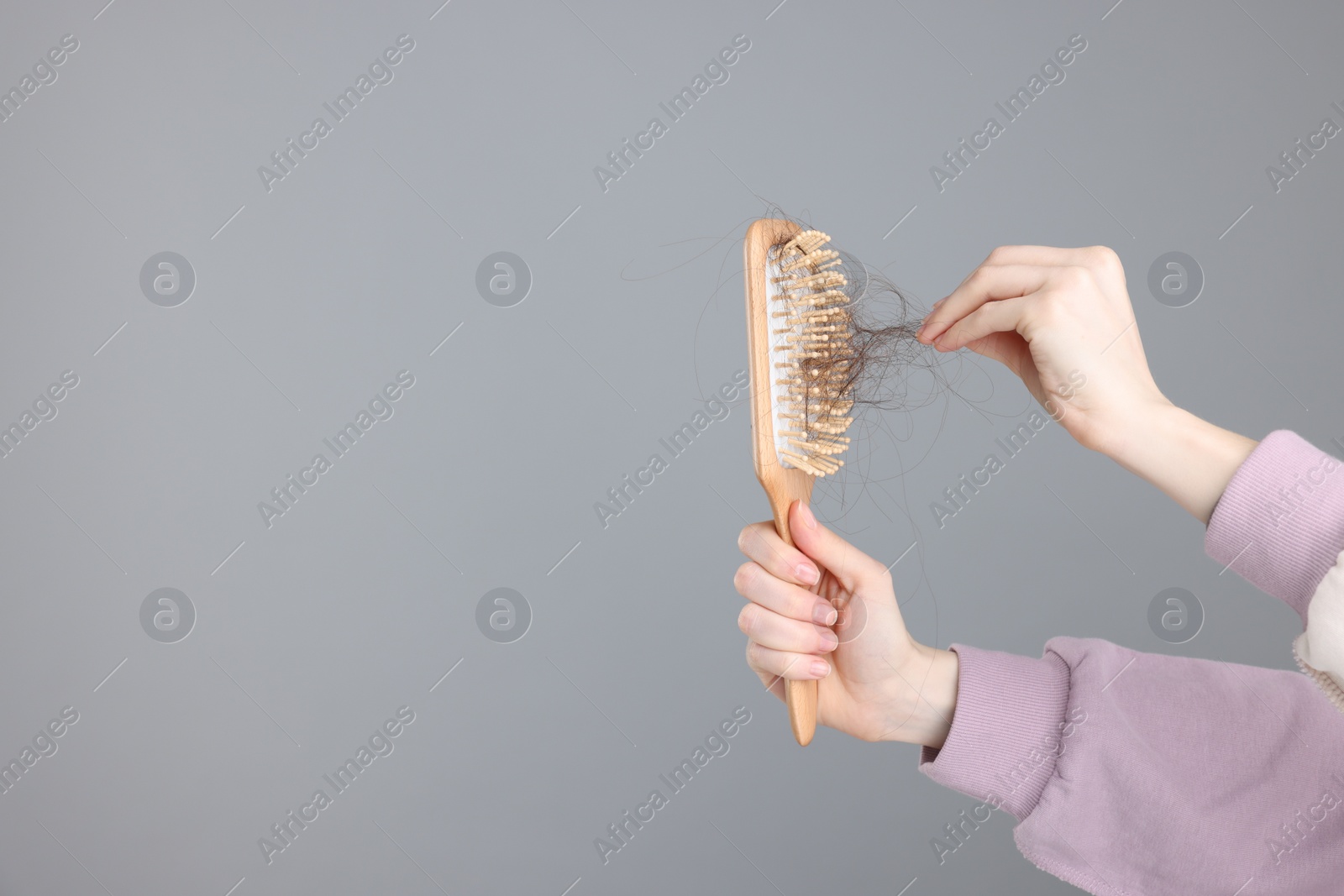 Photo of Woman holding brush with lost hair on light grey background, closeup and space for text. Alopecia problem