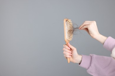 Photo of Woman holding brush with lost hair on light grey background, closeup and space for text. Alopecia problem