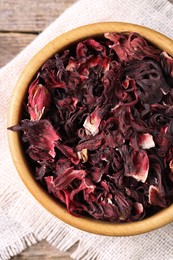 Photo of Dry hibiscus tea in bowl on wooden table, top view