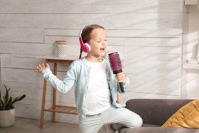 Photo of Cute little girl in headphones with hairbrush singing at home