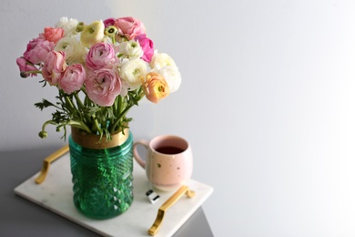 Photo of Bouquet of beautiful ranunculuses and tea on table near light grey wall. Space for text