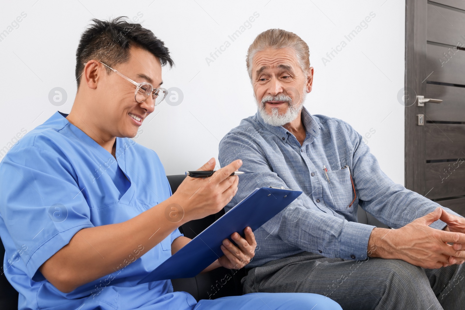 Photo of Doctor with clipboard consulting senior patient in clinic