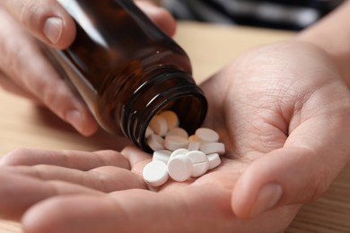Photo of Man pouring pills from bottle at wooden table, closeup