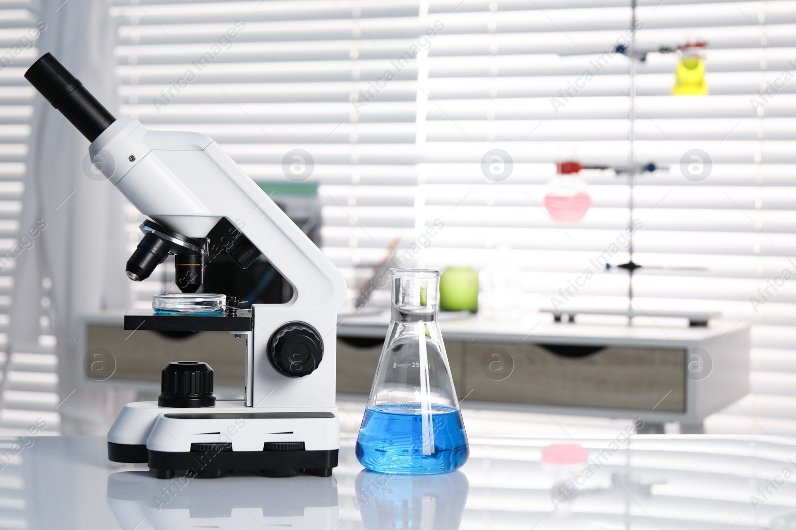 Photo of Laboratory analysis. Flask with blue liquid and microscope on white table indoors, space for text