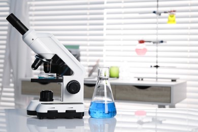 Laboratory analysis. Flask with blue liquid and microscope on white table indoors, space for text