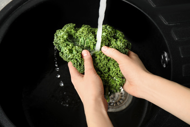 Woman washing fresh kale leaves over sink, closeup