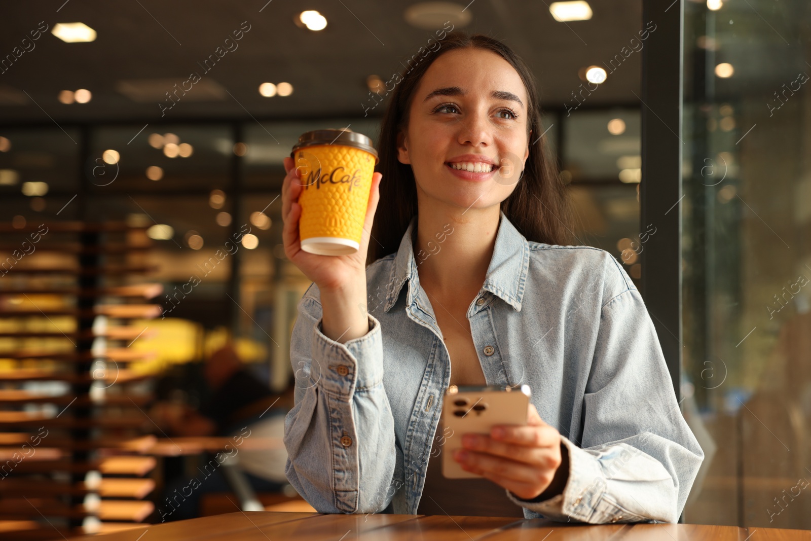 Photo of Lviv, Ukraine - September 26, 2023: Woman with hot McDonald's drink and smartphone in cafe