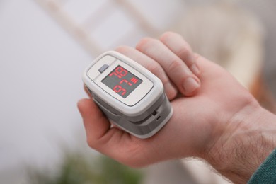 Photo of Man measuring oxygen level with modern fingertip pulse oximeter indoors, closeup