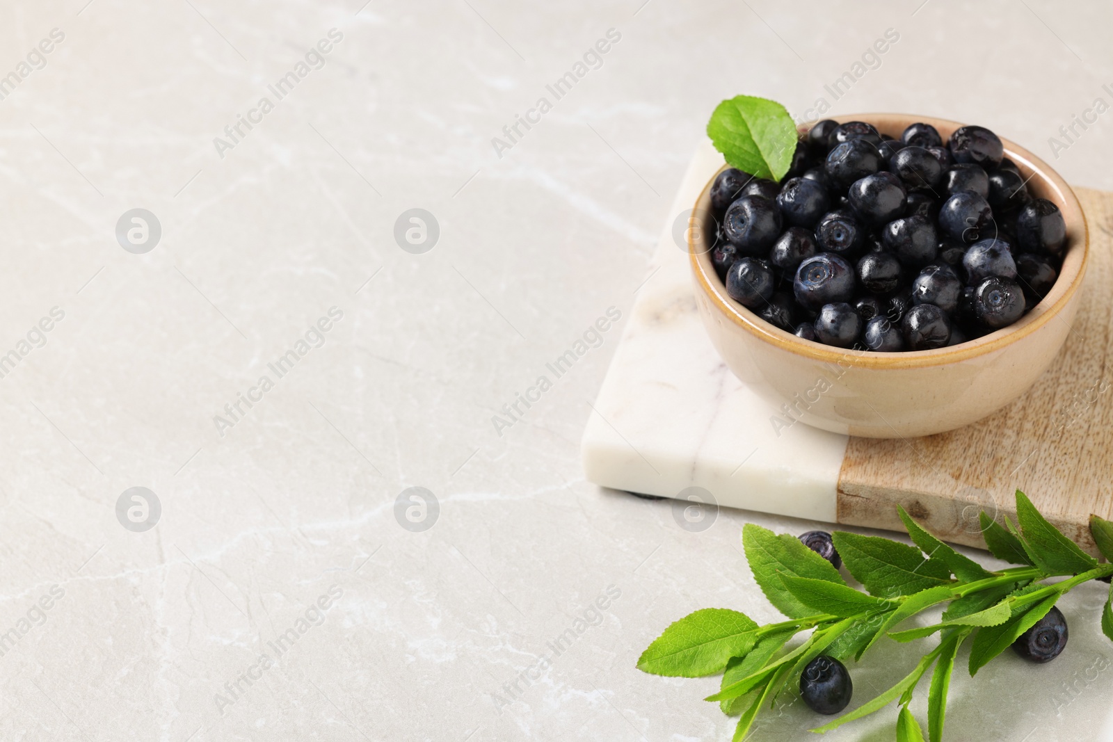 Photo of Bowl of tasty fresh bilberries and green leaves on white table. Space for text