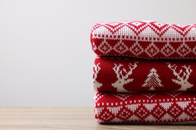 Photo of Stack of different Christmas sweaters on wooden table against light background. Space for text