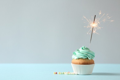 Photo of Delicious birthday cupcake with burning sparkler and space for text on light background