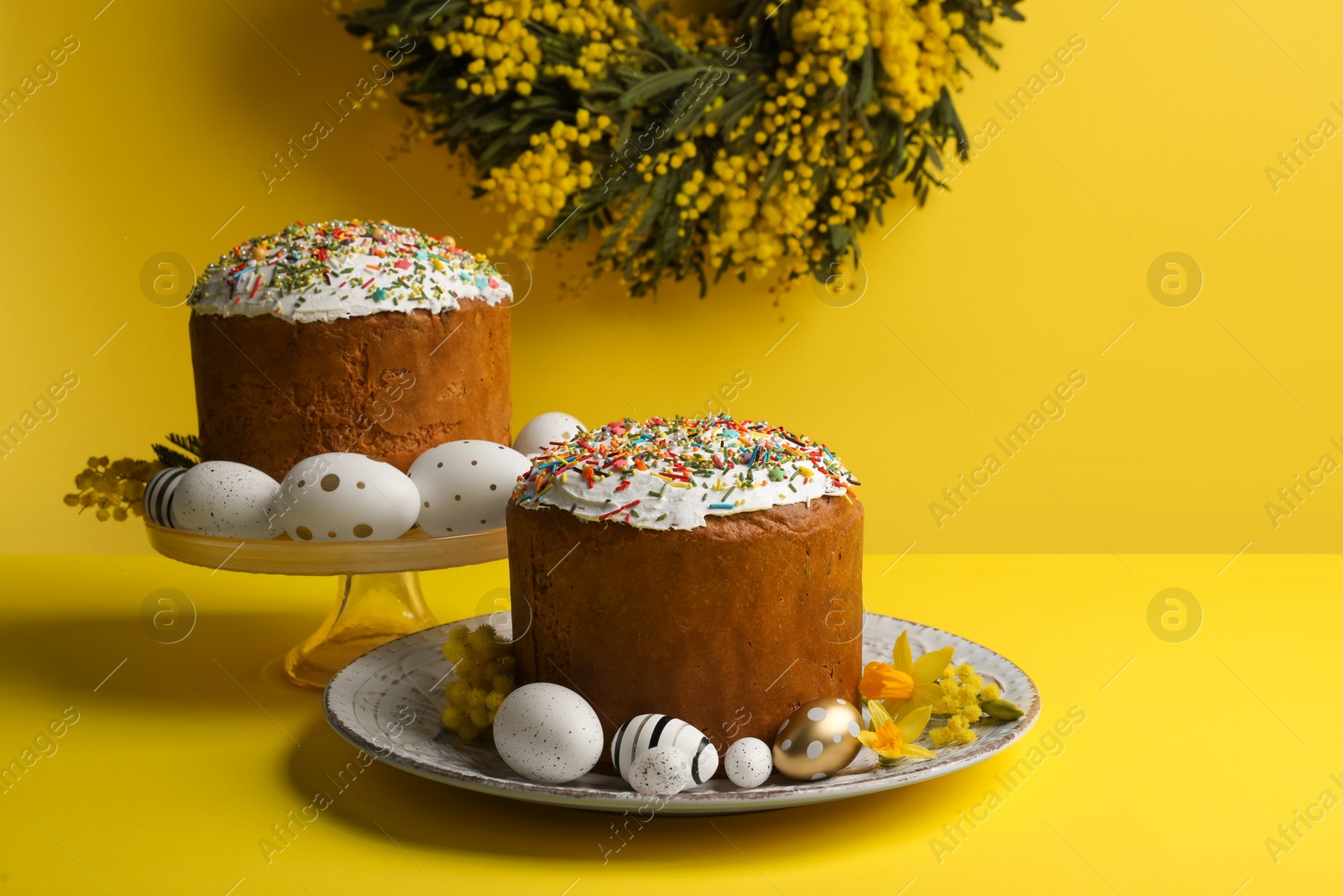 Photo of Traditional Easter cakes with sprinkles, painted eggs and beautiful spring flowers on yellow background