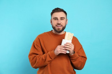 Young man with delicious shawarma on turquoise background
