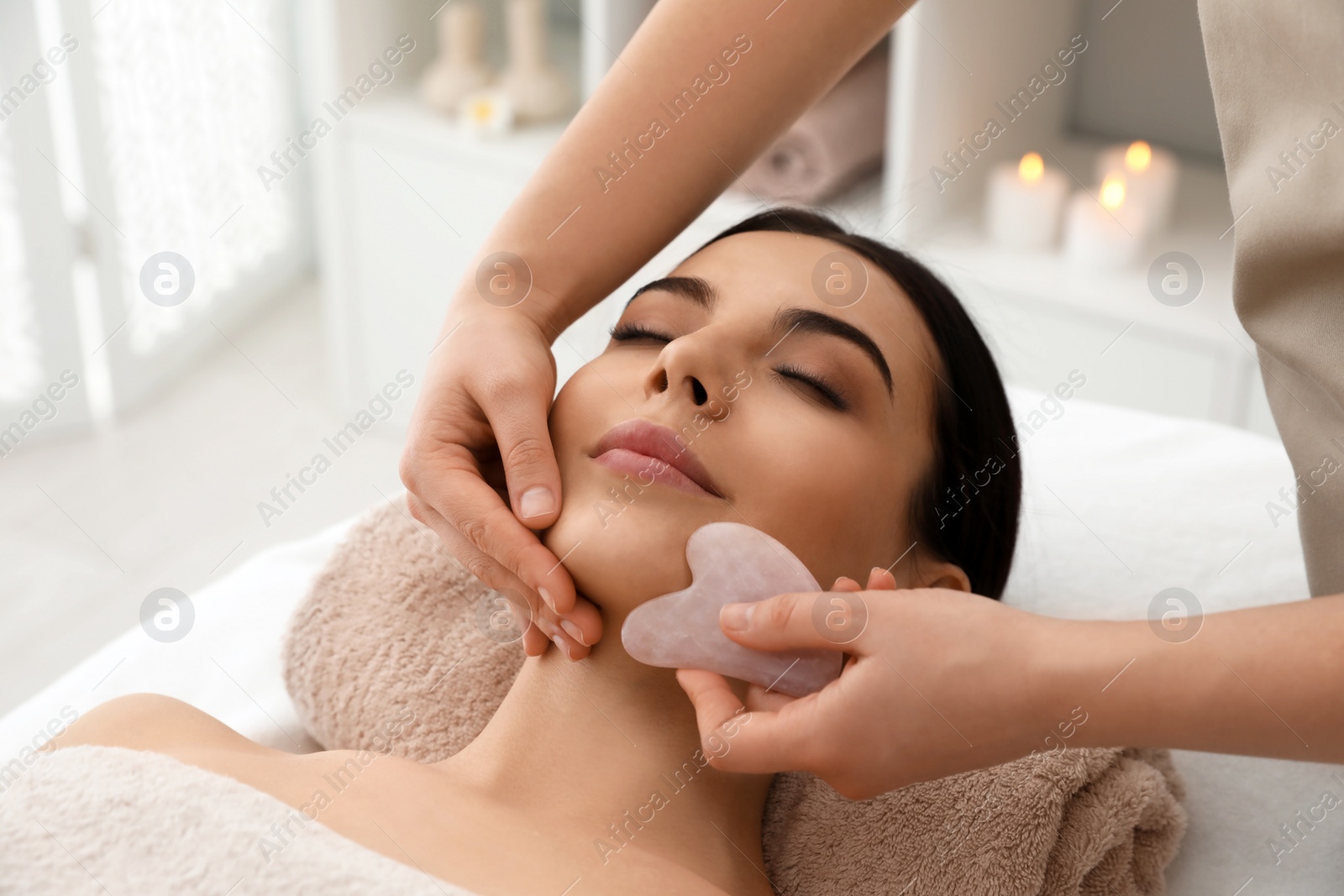 Photo of Young woman receiving facial massage with gua sha tool in beauty salon