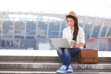 Photo of Beautiful woman with laptop sitting on stairs outdoors. Space for text