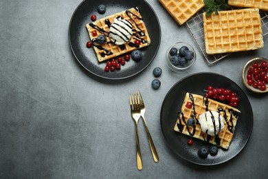 Photo of Delicious Belgian waffles with ice cream, berries and chocolate sauce on grey textured table, flat lay. Space for text