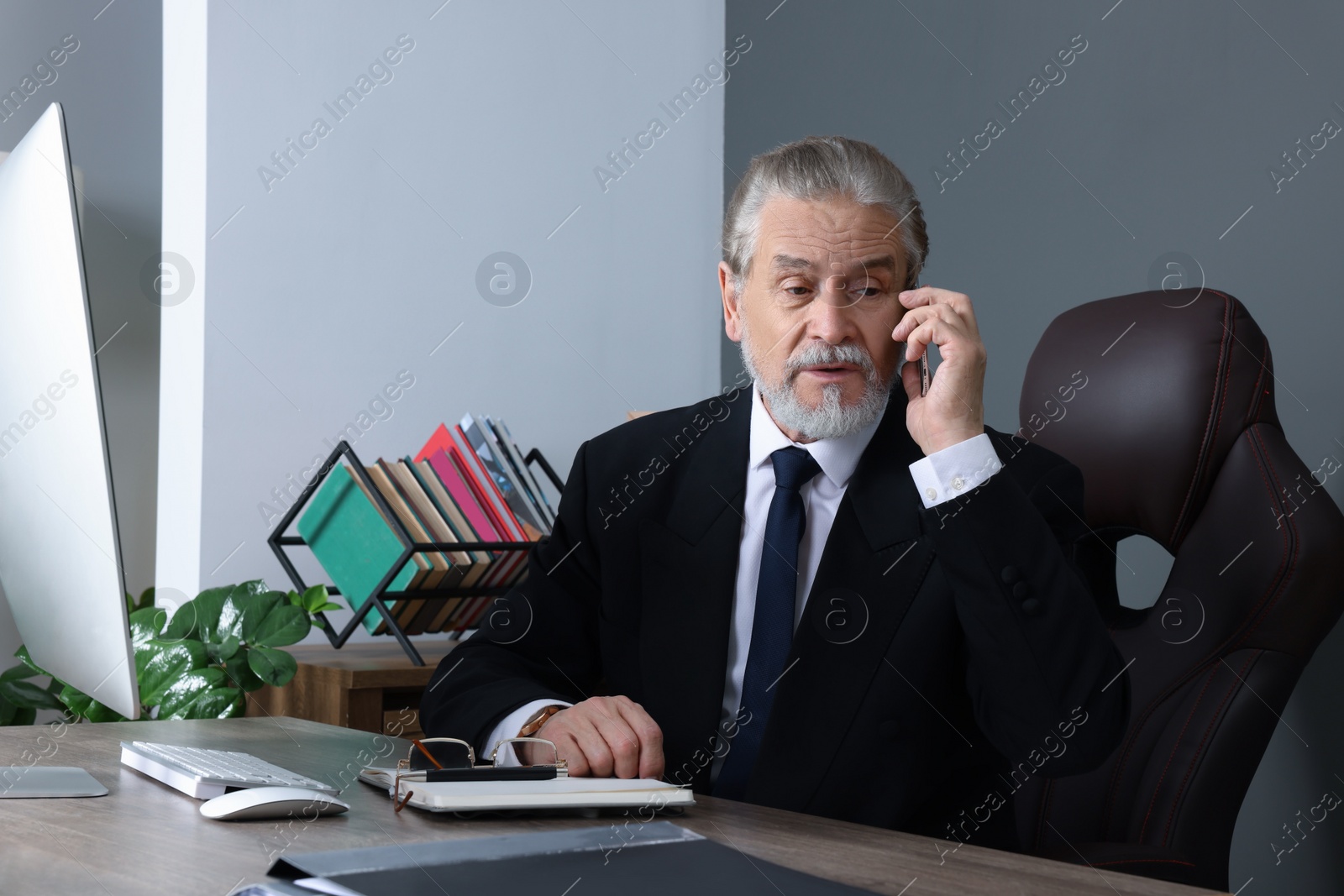 Photo of Emotional senior boss talking on phone at wooden table in modern office