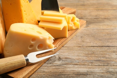 Photo of Different sorts of cheese and fork on wooden table, closeup. Space for text