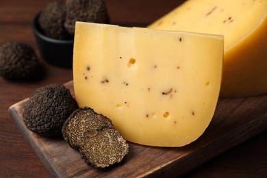 Photo of Delicious cheese and fresh black truffles on wooden board, closeup
