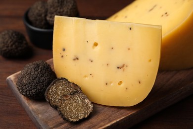 Delicious cheese and fresh black truffles on wooden board, closeup