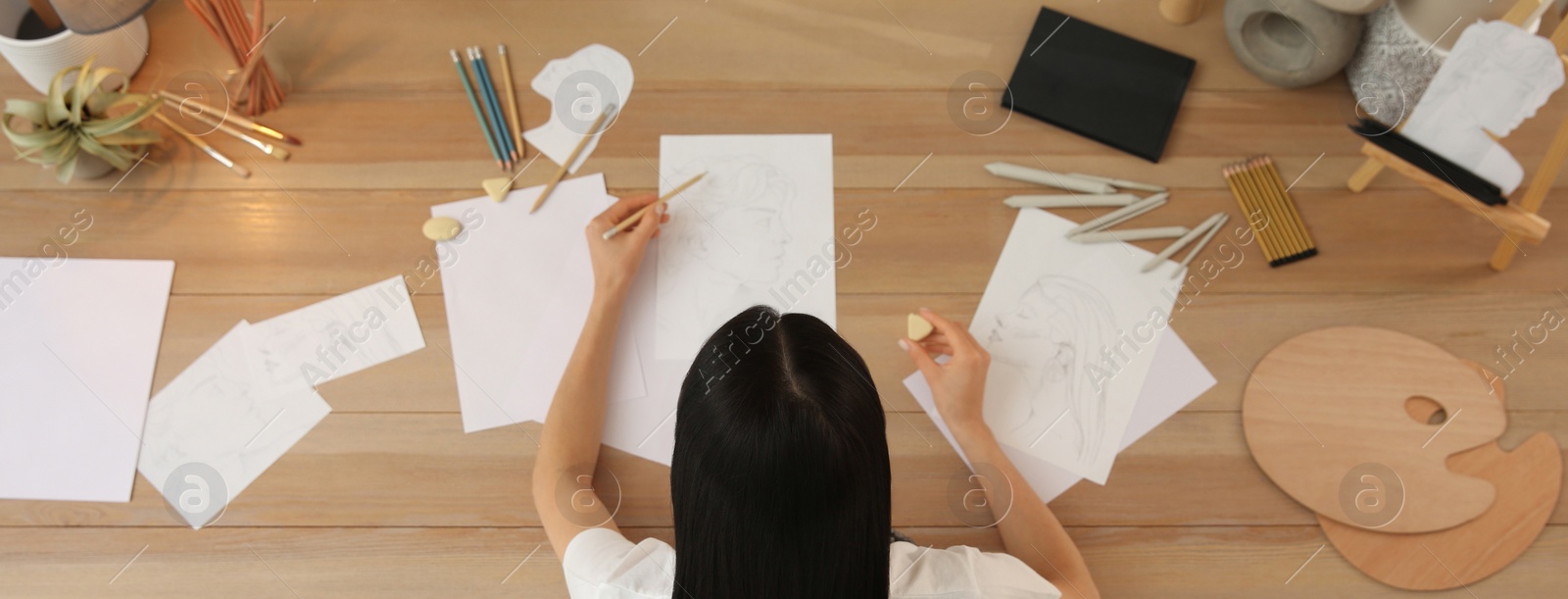 Image of Young woman drawing male portrait at table indoors, above view. Banner design
